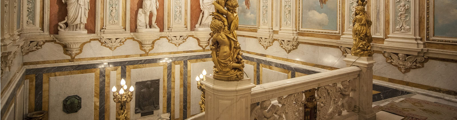 Vistas del interior del Palacio de Santoña, parte superior de la escalera principal, donde se aprecian altos techos y esculturas y murales.